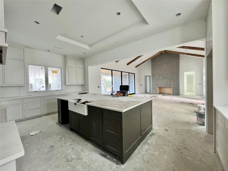 Kitchen featuring light stone countertops, lofted ceiling with beams, white cabinetry, and a spacious island