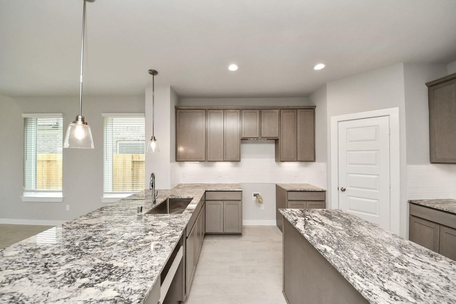 The kitchen is a culinary haven, featuring granite countertops, a tile backsplash, stainless steel appliances, 42” upper cabinets, and undercabinet lighting. Sample photo of completed home with similar floor plan. Actual colors and selections may vary. The kitchen is a culinary haven, featuring granite countertops, a tile backsplash, stainless steel appliances, 42” upper cabinets, and undercabinet lighting. Sample photo of completed home with similar floor plan. Actual colors and selections may vary.