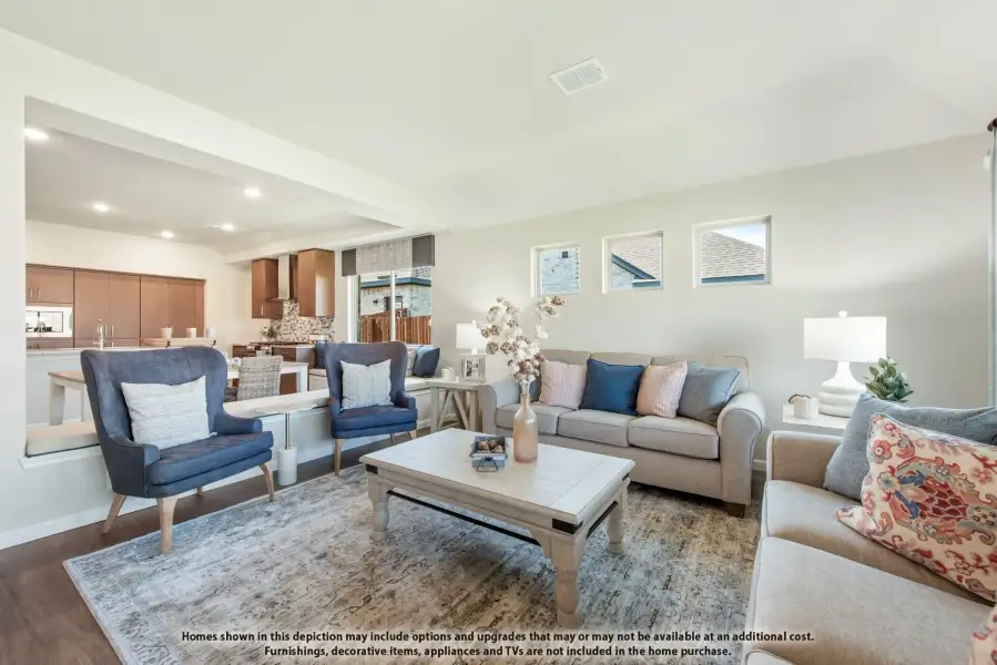 Open living room with beige sofas, blue accent chairs, and wood coffee table, open to kitchen beyond
