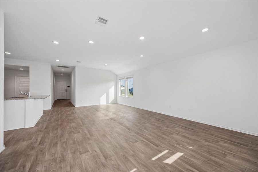 Spacious, open-plan living area with wood-style flooring, abundant natural light from a large window, and recessed lighting.
