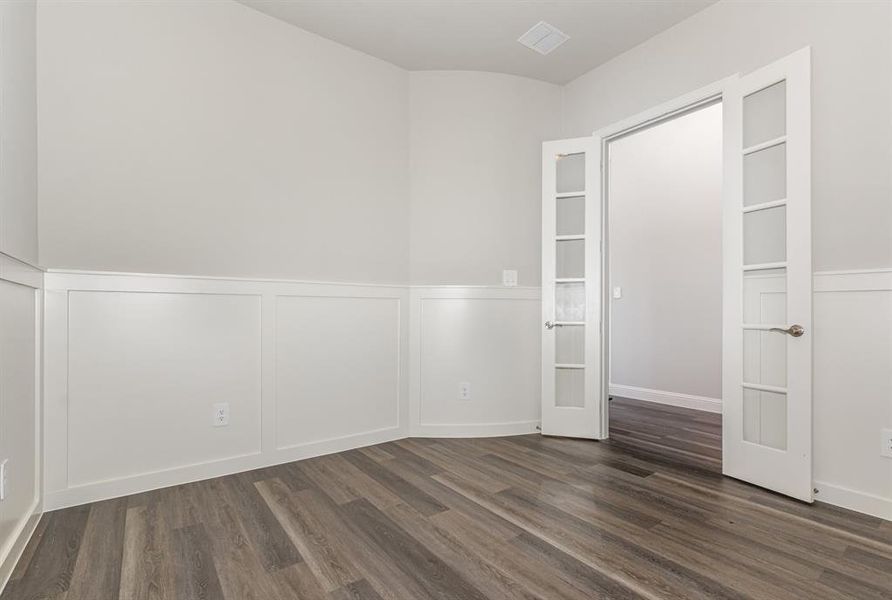 Empty room with wainscoting, a decorative wall, and dark wood-style flooring