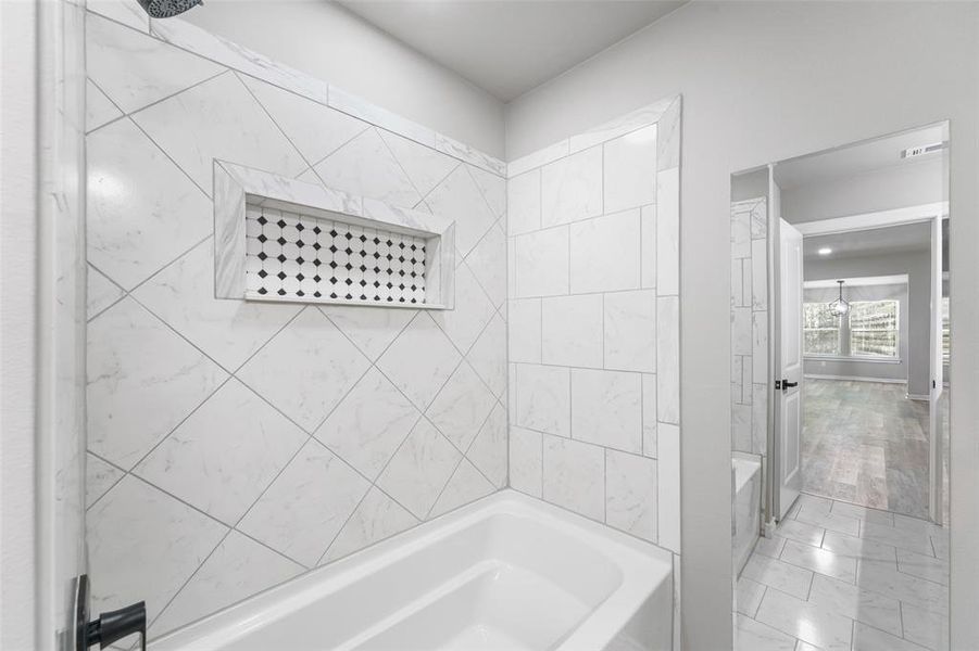 White ceramic tile bathtub surround with a decorative niche and black and white patterned tile insert, contrasting black shower fixtures, and light gray wall paint White ceramic tile bathtub surround with a decorative niche and black and white patterned tile insert, contrasting black shower fixtures, and light gray wall paint