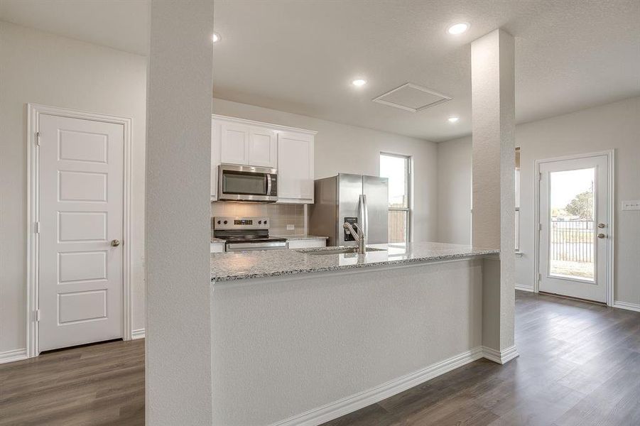Kitchen featuring light stone countertops, stainless steel appliances, white cabinetry, dark wood finished floors, and backsplash