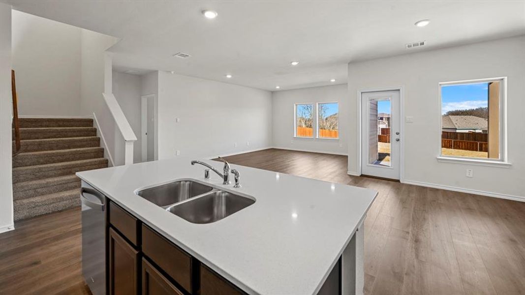 Kitchen island with a double basin sink and stainless steel faucet, dark wood-finish cabinetry, and light-toned countertops