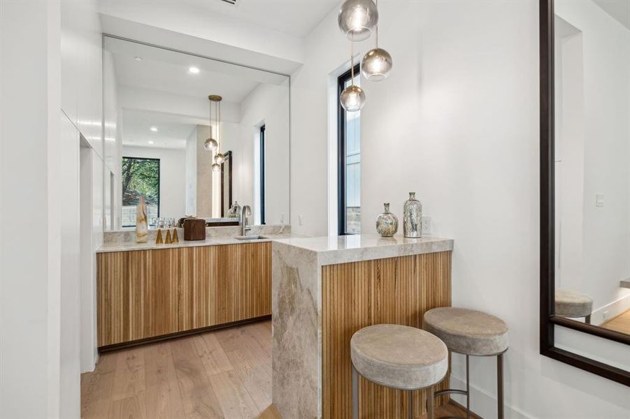 The wet bar is a sleek and functional space that is perfect for entertainingguests. Features include a large, Taj Mahal (quartzite natural stone) countertop with a sink and a modernfaucet, as well as wood paneling that covers the lower part of the countertop, adding a touch of warmthand texture.