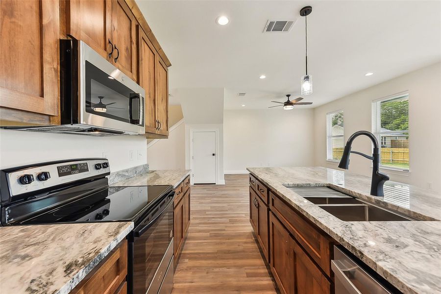 Kitchen with light wood look floors, stainless steel appliances, a sink, visible vents, and brown cabinetry Kitchen with light wood look floors, stainless steel appliances, a sink, visible vents, and brown cabinetry