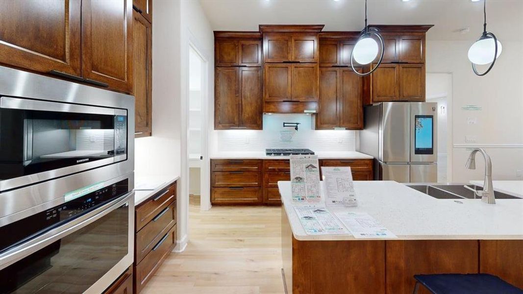 Kitchen with stainless steel appliances, light wood-style flooring, decorative backsplash, hanging light fixtures, and under cabinet range hood