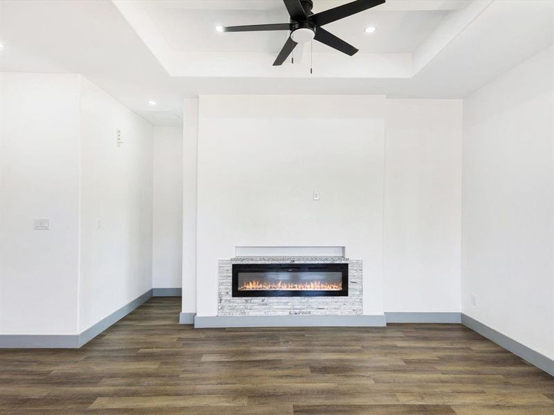 Unfurnished living room featuring a raised ceiling, a glass covered fireplace, dark wood-style floors, and recessed lighting Unfurnished living room featuring a raised ceiling, a glass covered fireplace, dark wood-style floors, and recessed lighting