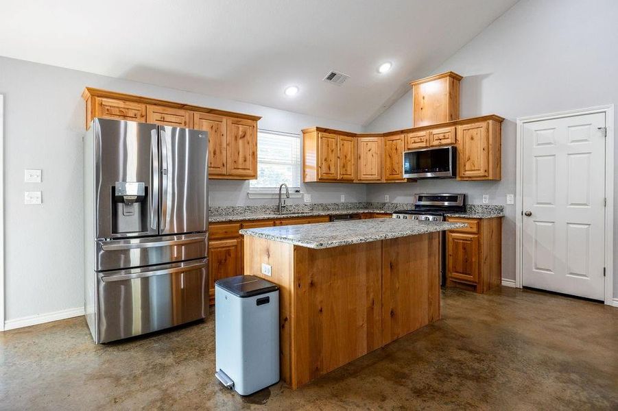 Kitchen featuring light stone countertops, stainless steel appliances, brown cabinetry, a center island, and recessed lighting