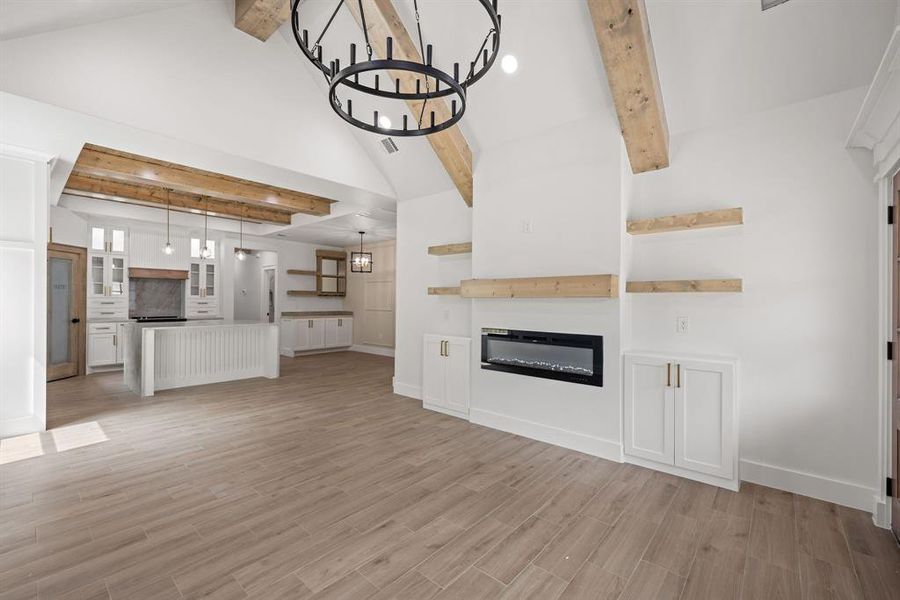 Vaulted ceiling with exposed wood beams, wood-finish flooring, built-in electric fireplace, recessed lighting, and a kitchen featuring a center island with pendant lighting