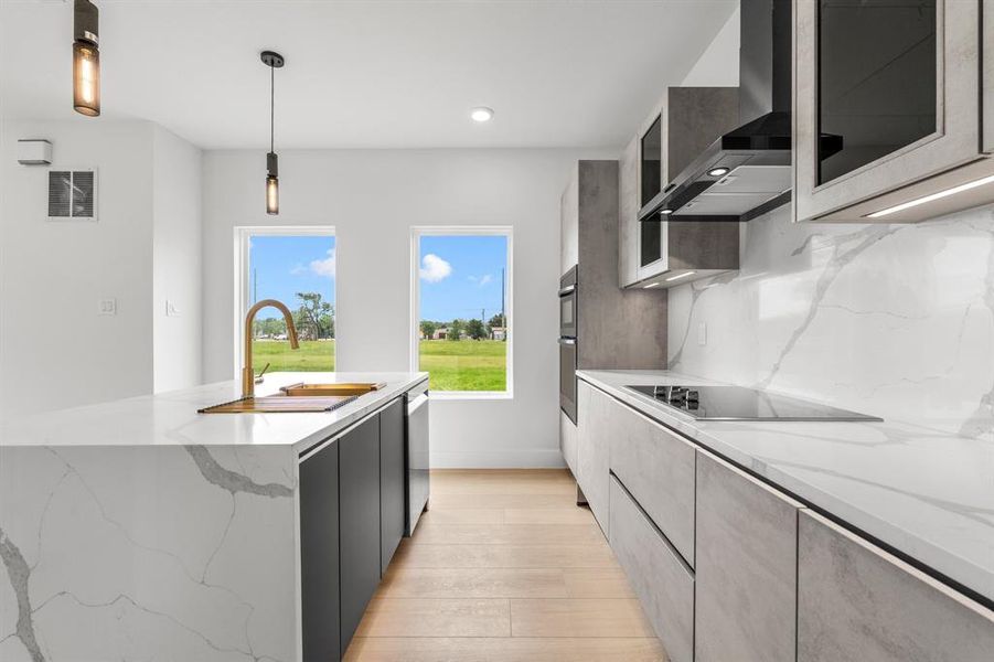 Kitchen featuring visible vents, a sink, light wood-style floors, wall chimney exhaust hood, and black electric stovetop