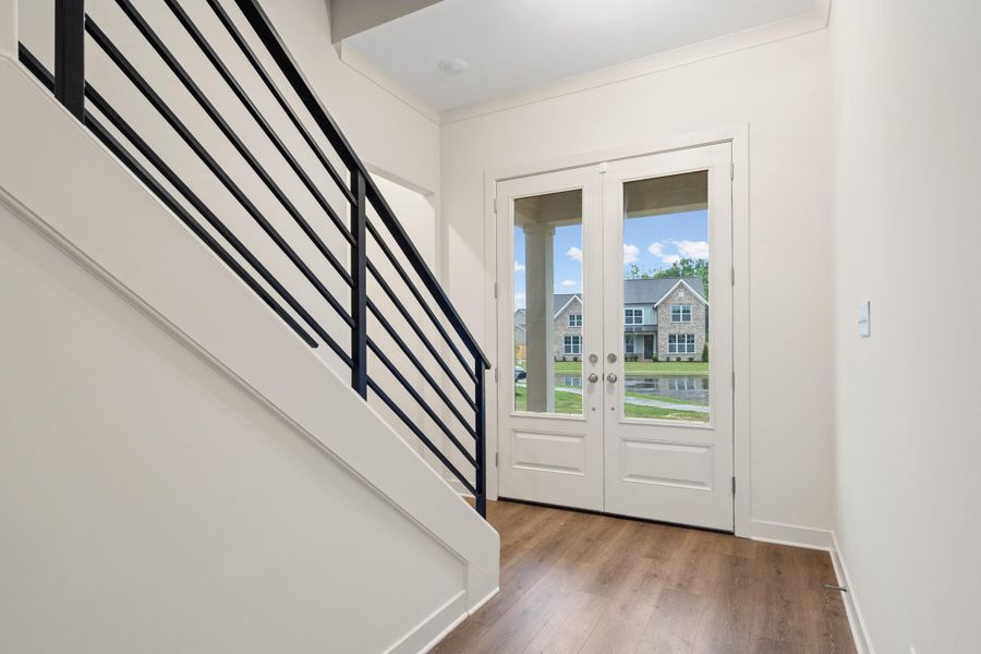 Entry foyer featuring wood-finish flooring, a modern black metal staircase railing, and double glass-paneled entry doors Entry foyer featuring wood-finish flooring, a modern black metal staircase railing, and double glass-paneled entry doors