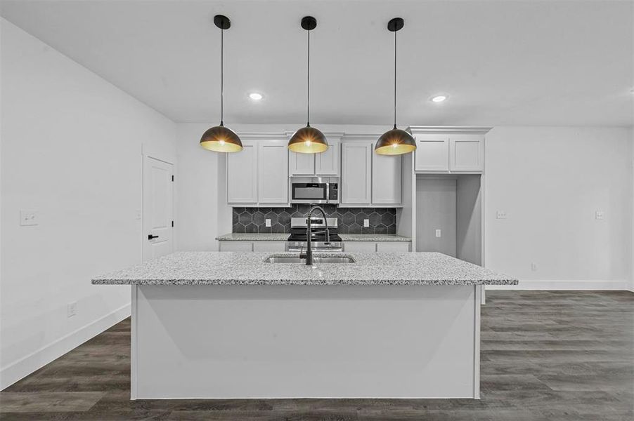 Kitchen featuring white cabinetry, decorative light fixtures, light stone counters, sink, and a center island with sink