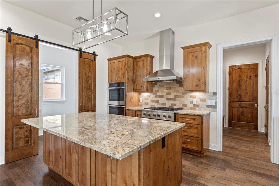 Kitchen with wall chimney range hood, a barn door, a center island, dark wood-style floors, and recessed lighting