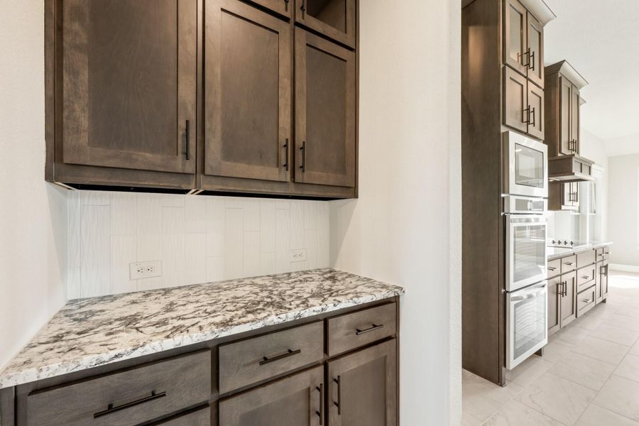 Kitchen with dark brown cabinets, granite countertops, white tile backsplash, and built-in double ovens visible in background.