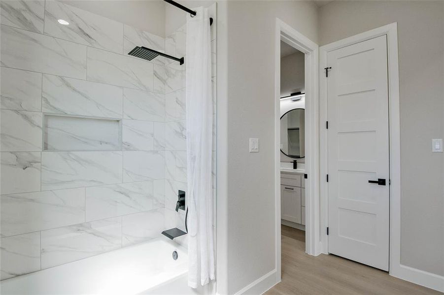 Full bathroom featuring shower / bath combination with curtain, vanity, and light wood finished floors Full bathroom featuring shower / bath combination with curtain, vanity, and light wood finished floors