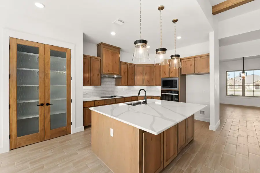 Kitchen with brown cabinets, pendant lighting, a kitchen island with sink, wood finish floors, and recessed lighting