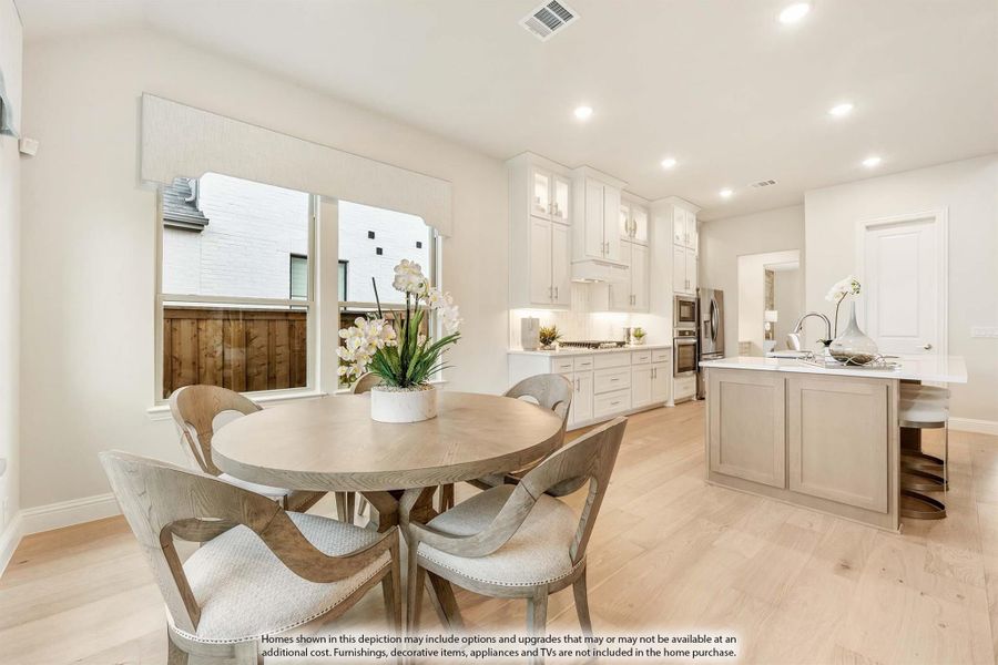 Open dining area with round wood table flowing into kitchen with white cabinets and center island