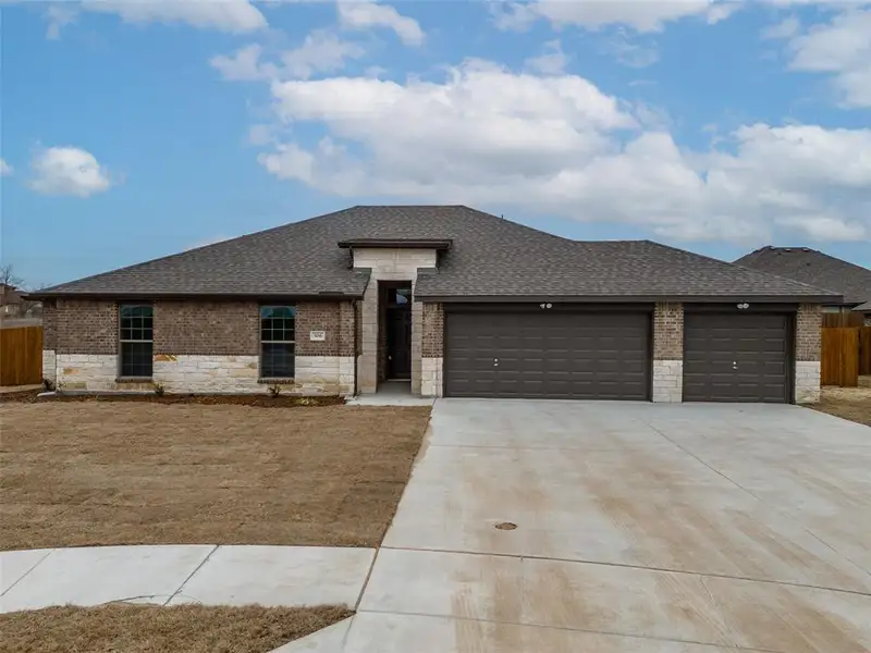 Prairie-style home with an attached garage, a shingled roof, fence, and brick siding