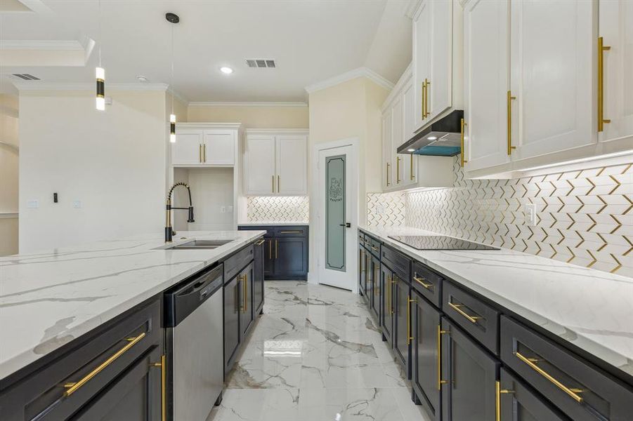 Kitchen featuring light stone counters, dual tone cabinets, stainless steel dishwasher, light marble finish flooring, and pendant lighting