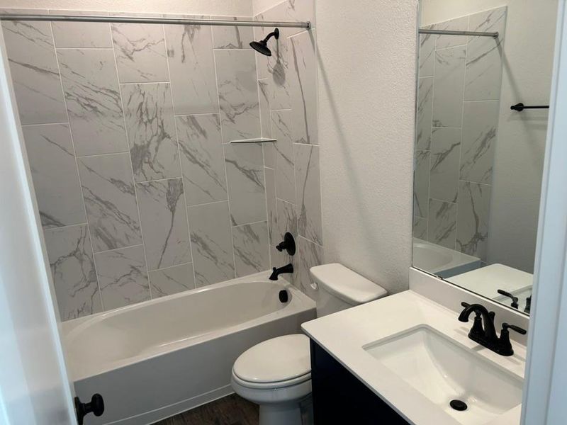 Full bathroom with bathing tub / shower combination, vanity, a textured wall, and dark wood-style flooring Full bathroom with bathing tub / shower combination, vanity, a textured wall, and dark wood-style flooring