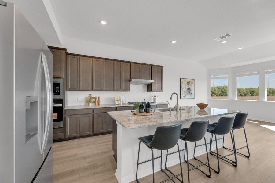 Kitchen featuring stainless steel appliances, light stone counters, a kitchen breakfast bar, light wood finished floors, and recessed lighting Kitchen featuring stainless steel appliances, light stone counters, a kitchen breakfast bar, light wood finished floors, and recessed lighting