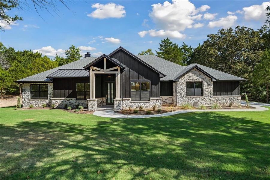 Modern inspired farmhouse with stone siding, board and batten siding, a front yard, and a chimney