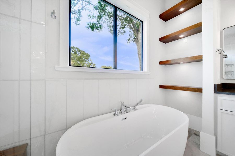 The primary ensuite features a soaking tub and accent lit shelving.