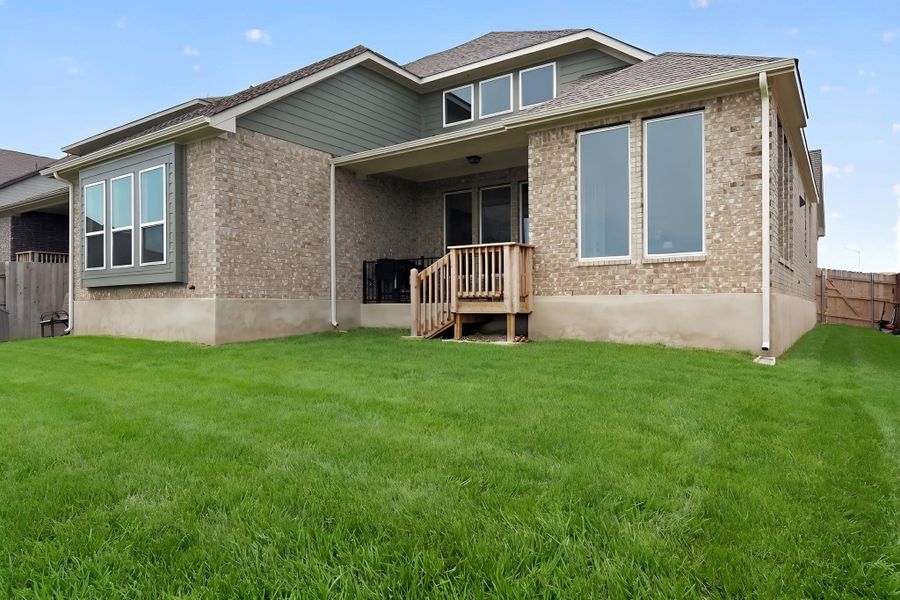 Spacious backyard featuring a manicured lawn, brick facade, covered patio, and multi-pane windows Spacious backyard featuring a manicured lawn, brick facade, covered patio, and multi-pane windows