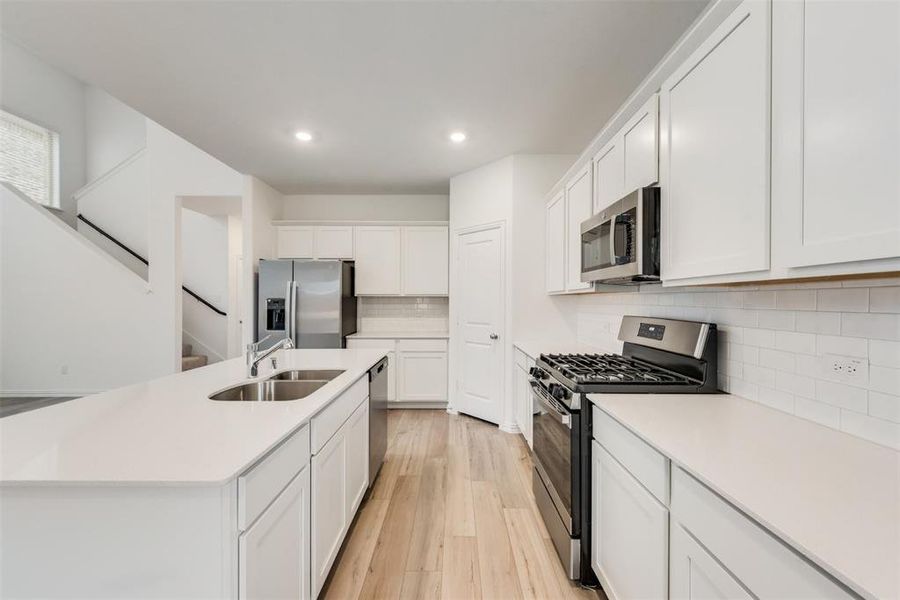 Kitchen featuring a center island with sink, light hardwood / wood-style flooring, stainless steel appliances, sink, and white cabinets