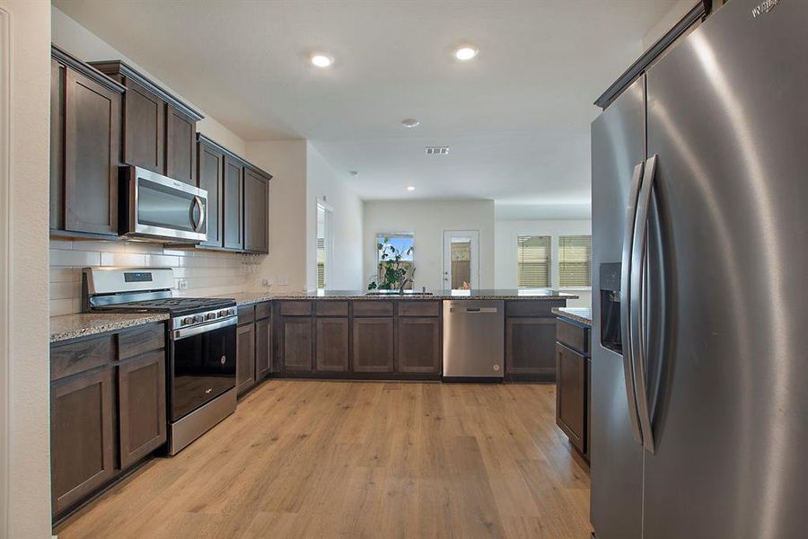 Kitchen with kitchen peninsula, decorative backsplash, dark brown cabinets, appliances with stainless steel finishes, and light hardwood / wood-style flooring