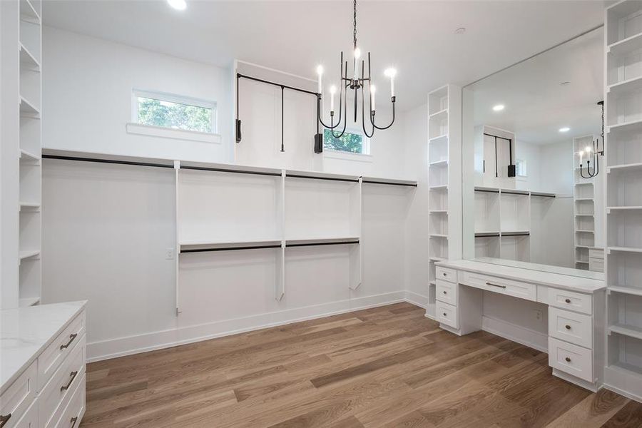 Spacious closet featuring built in desk, a chandelier, and light wood-type flooring