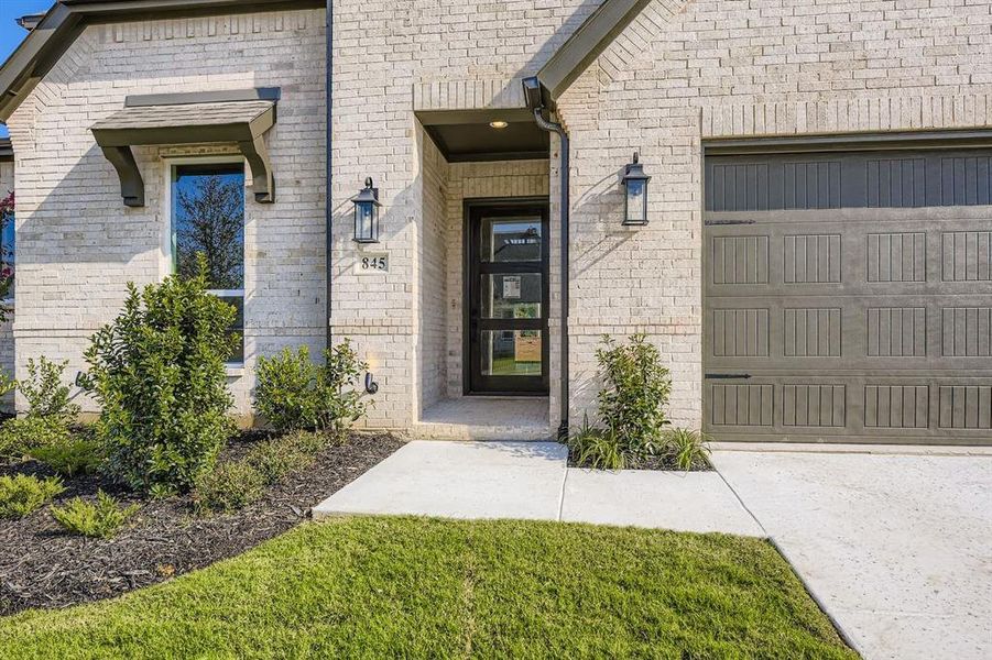 Entrance to property with brick siding, a lawn, and an attached garage Entrance to property with brick siding, a lawn, and an attached garage