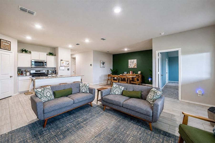 Open-concept living space featuring wood-finish flooring, recessed lighting, a kitchen with white cabinetry and stainless steel appliances, and a distinct dining area with an accent wall
