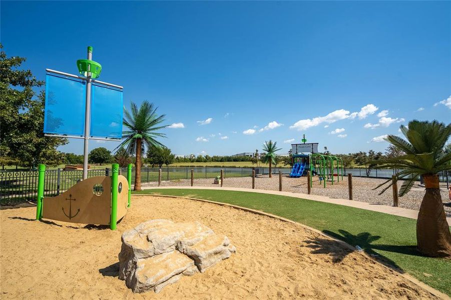 Playground area featuring a sandpit, ship-themed play structure with blue sails, artificial turf pathways, and various playground equipment Playground area featuring a sandpit, ship-themed play structure with blue sails, artificial turf pathways, and various playground equipment