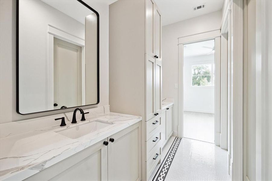 The shared bathroom for the 3rd and 4th bedrooms with custom cabinetry, double vanities and a shower/tub combo. The tile floor features a black patterned border that provides a vintage touch.