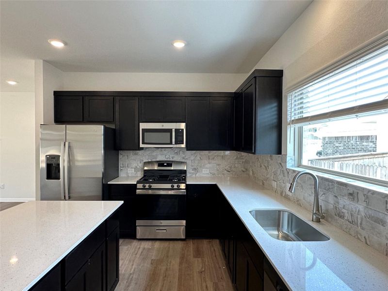 Kitchen featuring dark cabinetry, light stone countertops, appliances with stainless steel finishes, backsplash, and recessed lighting