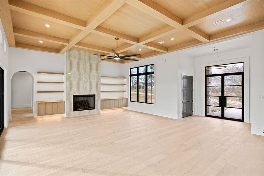 Unfurnished living room with beam ceiling, coffered ceiling, light wood-style floors, a premium fireplace, and a ceiling fan