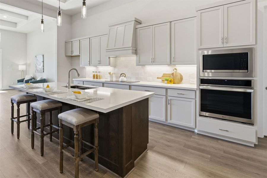 Kitchen featuring stainless steel appliances, a breakfast bar, two tone cabinets, light wood-style floors, and hanging light fixtures