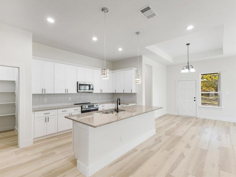 Kitchen with light wood-type flooring, decorative backsplash, a center island with sink, stainless steel appliances, and a tray ceiling