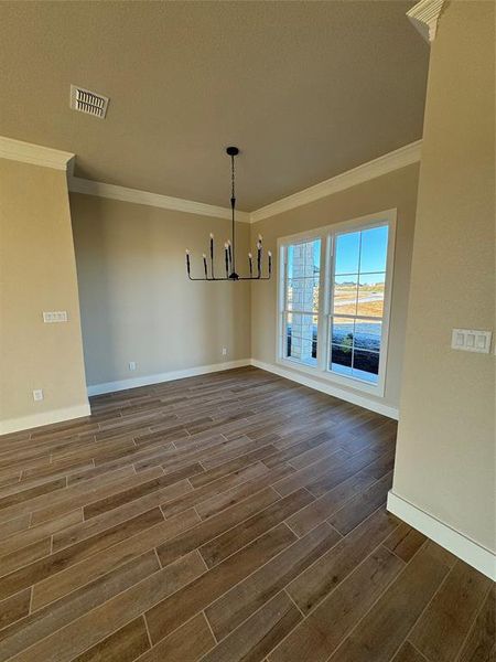 Unfurnished dining area featuring a textured ceiling, a notable chandelier, crown molding, and dark wood-type flooring