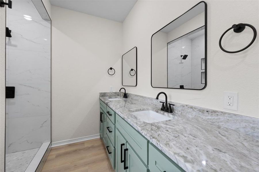 Full bath with double vanity, light wood-type flooring, and a marble finish shower