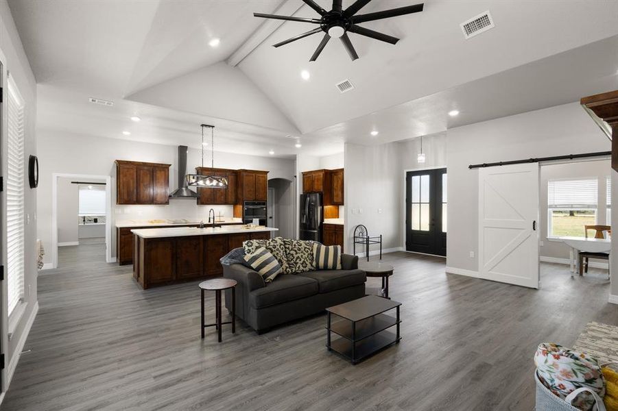 Living room featuring a barn door, beamed ceiling, a ceiling fan, dark wood-style floors, and high vaulted ceiling