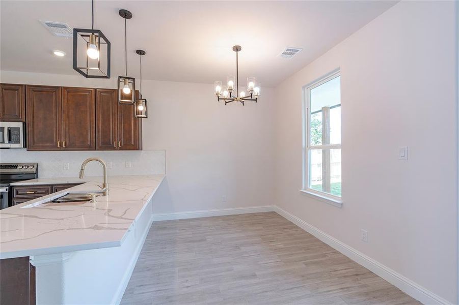 Kitchen featuring light hardwood / wood-style flooring, hanging light fixtures, kitchen peninsula, a chandelier, and appliances with stainless steel finishes