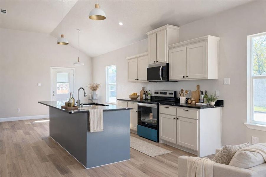 Kitchen with stainless steel appliances, a kitchen island with sink, light wood-style flooring, decorative light fixtures, and vaulted ceiling