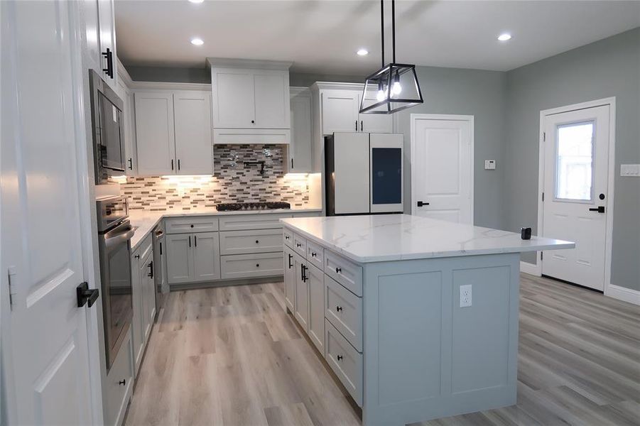 Kitchen featuring backsplash, light stone countertops, a kitchen island, pendant lighting, and recessed lighting