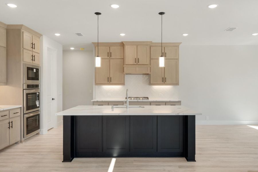 Kitchen with large dark island, white countertops, light wood cabinets, and double wall ovens