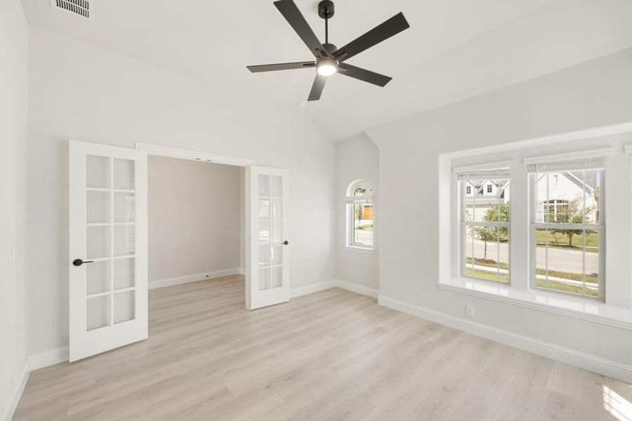 Empty room with vaulted ceiling, ceiling fan, French doors, and light hardwood floors