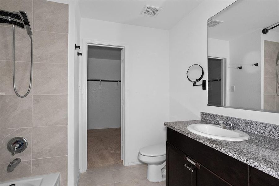 Full bath featuring  shower combination, vanity, light tile patterned flooring, and a walk in closet