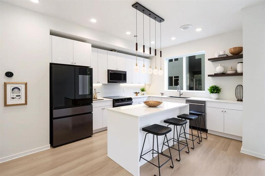 Kitchen featuring black appliances, white cabinets, a breakfast bar, a kitchen island, and light wood-type flooring